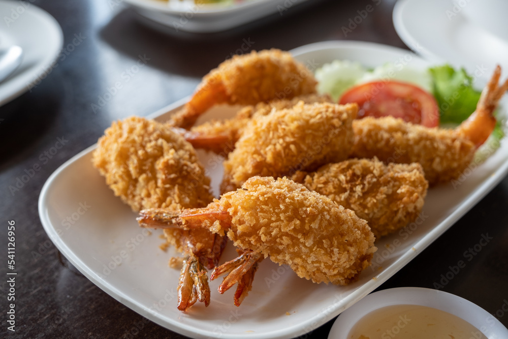 The whole fried chicken is chopped into pieces and placed in a white plate placed on the table. The whole fried chicken is chopped into pieces and placed in a white plate placed on the table.