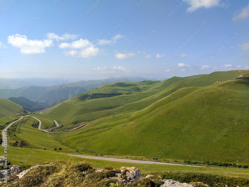 Beautiful view of the Caucasus mountains and green hills against the blue sky. The serpentine road goes into the distance. Prielbrusye National Park, Kabardino-Balkaria, Caucasus, Russia