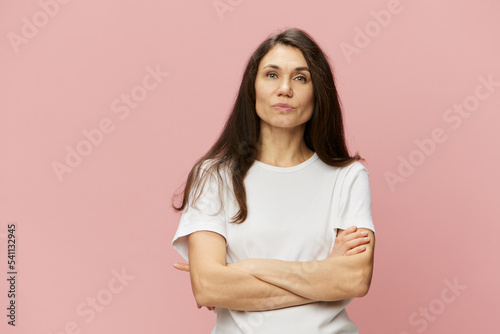 horizontal portrait on a pink background of a happy woman with her arms crossed on her chest in a white cotton T-shirt