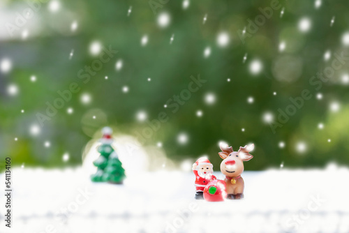 santa doll, reindeer and presents with snow decorated background green nature. concept christmas celebration, santa claus deliver presents on snowy day