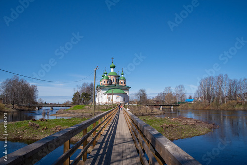 View of the Cathedral of the Smolensk Icon of the Mother of God and the old wooden bridge on the Megrega river on a sunny. Olonets, Karelia photo