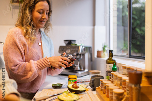 woman opening a beeswax wrap in the kitchen with avocado and spices on the bench photo