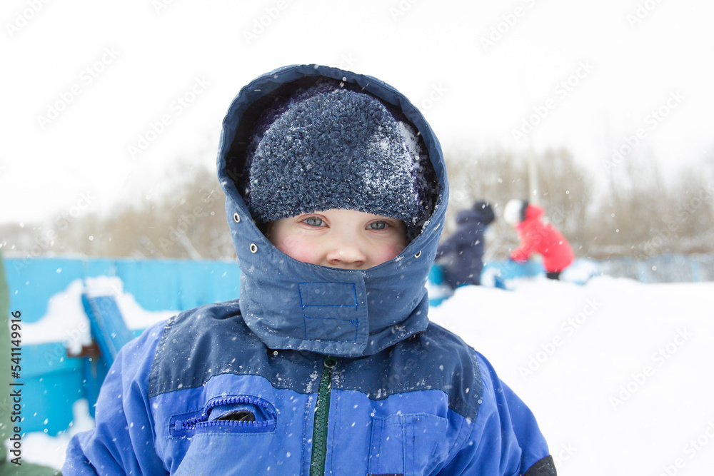 A little boy wrapped in warm clothes on a winter day looks at the camera. The arrival of winter. A beautiful child with blue eyes in a snowy hat. A little boy wrapped in warm clothes on a winter day looks at the camera. The arrival of winter. A beautiful child with blue eyes in a snowy hat.
