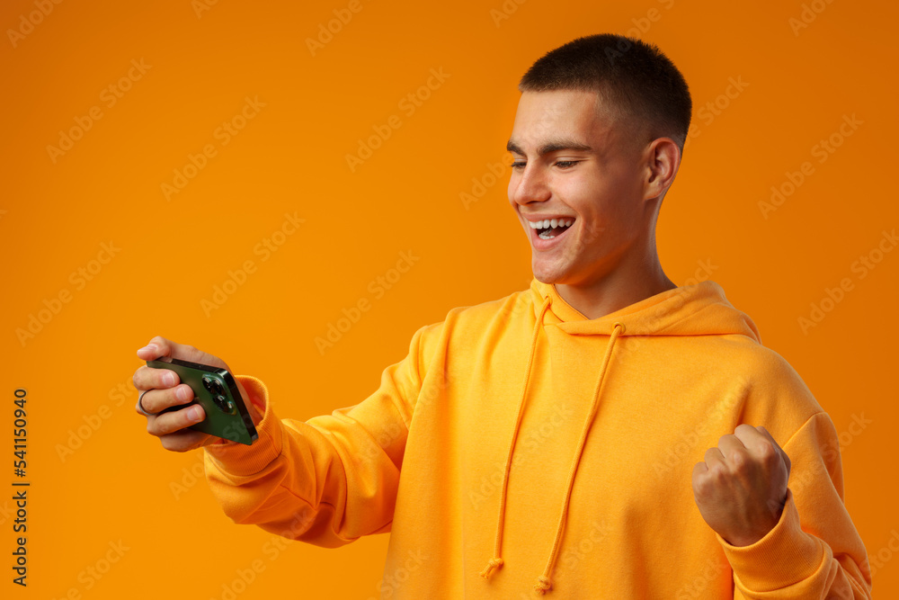 Portrait of excited young man playing online game on mobile phone on yellow background. Portrait of excited young man playing online game on mobile phone on yellow background.