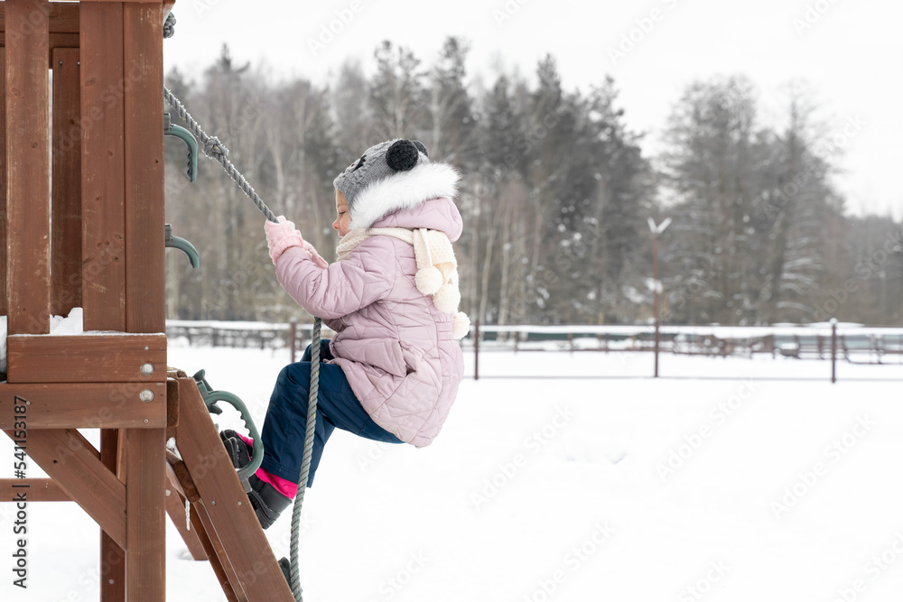 a child on a playground in winter climbs a rope a child on a playground in winter climbs a rope