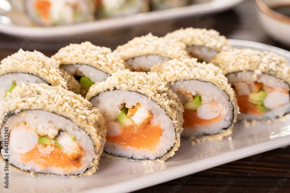 Hot tempura sushi rolls with cream cheese on white dish on black background. Japanese traditional fusion food style, Sushi menu. Japanese food. Futomaki Hot tempura sushi rolls with cream cheese on white dish on black background. Japanese traditional fusion food style, Sushi menu. Japanese food. Futomaki