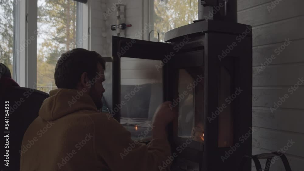 Young Man starts fire in wood burning stove inside Nordic countryside cabin Young Man starts fire in wood burning stove inside Nordic countryside cabin