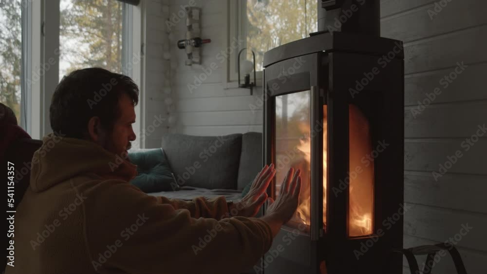 Man sits in front of indoor fireplace warming his cold hands - Medium close