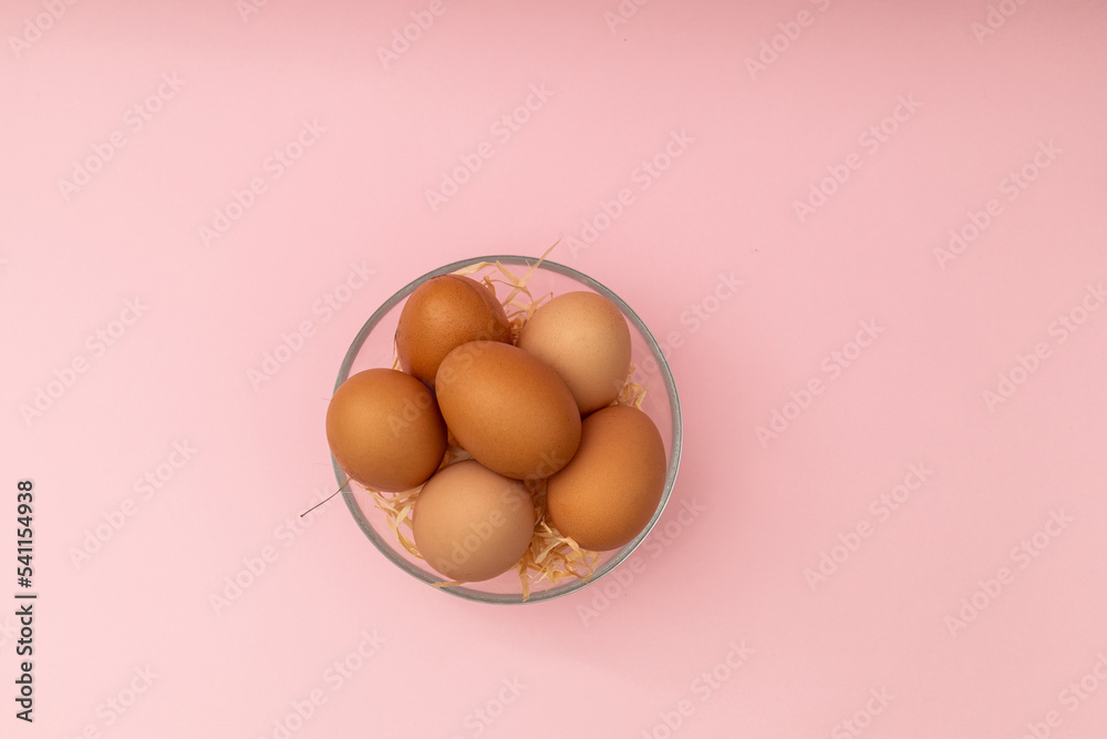 Chicken eggs in a transparent plate on a pink background