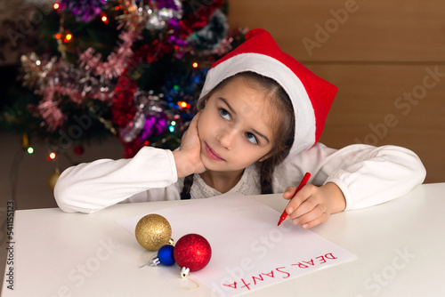 Cute little girl in Santa hat is writing a letter to Santa Claus on Christmas