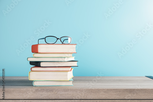 Close up of stacked books and glasses on blurry blue background with mock up place. School and education concept. 3D Rendering. photo