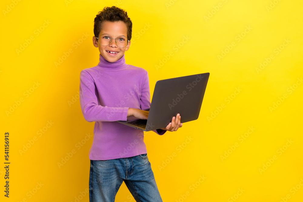 Portrait of cheerful smart schoolchild hols use wireless netbook isolated on yellow color background Portrait of cheerful smart schoolchild hols use wireless netbook isolated on yellow color background