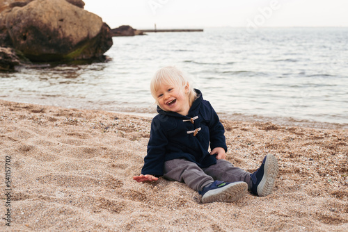 baby boy sitting on sand on beach in autumn time © Marharyta