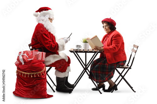 Santa Claus using smartphonr and an elderly woman sitting at a table and reading book photo