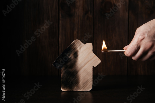 Fotografia Wooden house and hand with match. Fire and real estate concept