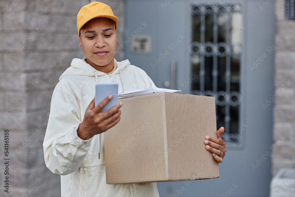 Waist up portrait of multiethnic young woman delivering packages and using smartphone, copy space Waist up portrait of multiethnic young woman delivering packages and using smartphone, copy space