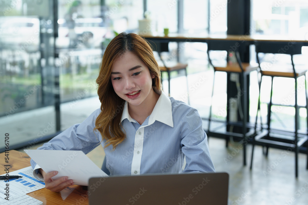 Portrait of a thoughtful Asian businesswoman looking at financial statements and making marketing plans using a computer on her desk Portrait of a thoughtful Asian businesswoman looking at financial statements and making marketing plans using a computer on her desk