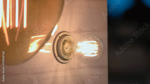 Hand switches off light bulb on the wall. Turning of glowing incandescent bulb. photo