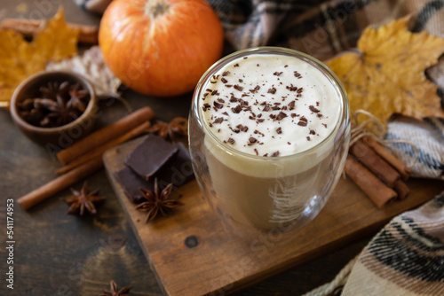 Pumpkin latte spice coffee, warm scarf and maple leaves on rustic background. Seasonal autumn concept with hot drink.