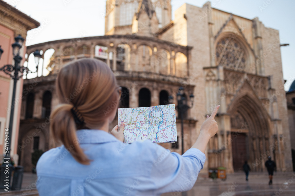 Young traveller woman walking on old town holding tourist map looking for direction in the city. Valencia, Spain travel summer tourism holiday vacation background. Back view