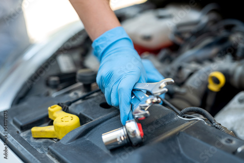 hands of a female mechanic working under the hood of a car in a car service.