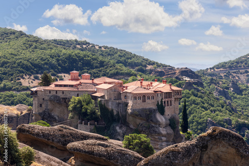 Red tiled roofs, chimneys and ornamented arched windows of religious medieval buildings of The Holy St Varlaam Monastery in Meteora, Greece © Artem