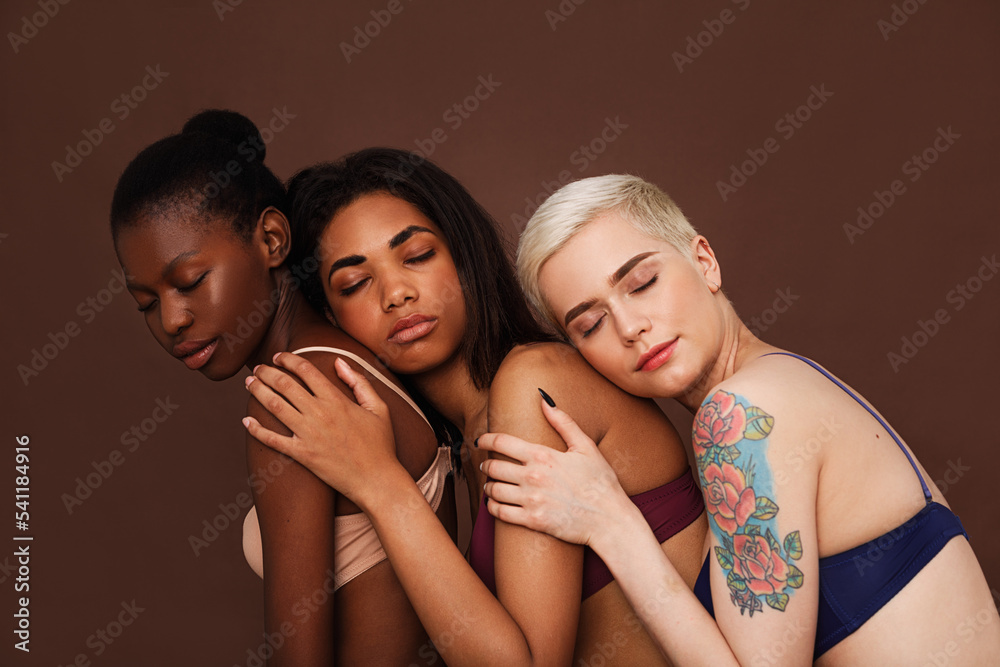 Three women in lingerie with closed eyes against a brown backdrop. Diverse females are embracing together. Three women in lingerie with closed eyes against a brown backdrop. Diverse females are embracing together.