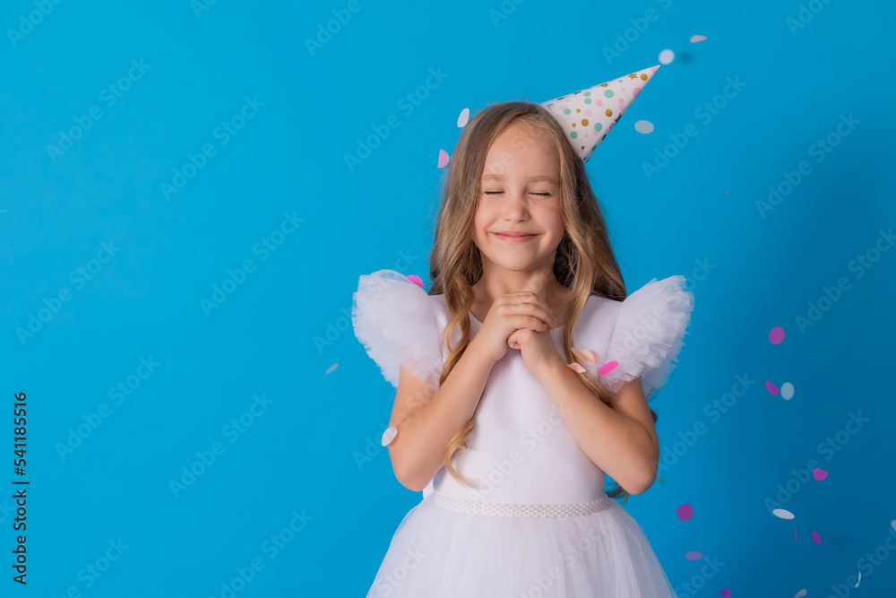 girl in a beautiful dress and a cardboard hat stands on a blue background and throws confetti girl in a beautiful dress and a cardboard hat stands on a blue background and throws confetti