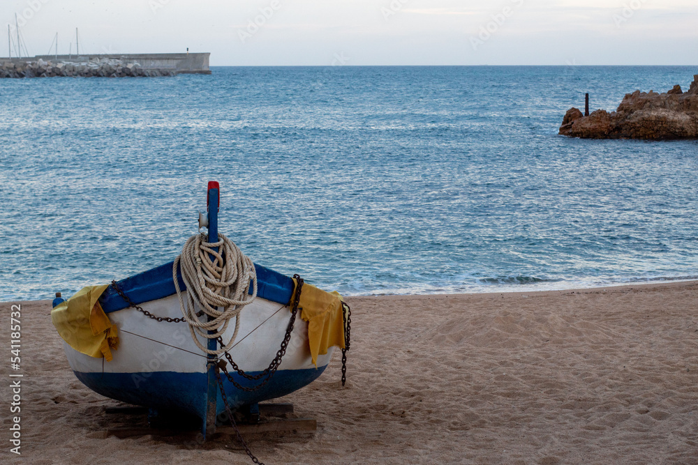 Solitaria barquita de pesca amarrada en la fina arena de la orilla en playa de Blanes con el tranquilo y azul mar de fondo .