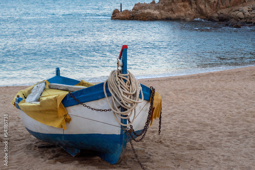 Solitaria barquita de pesca amarrada en la fina arena de la orilla en playa de Blanes con el tranquilo y azul mar de fondo . photo