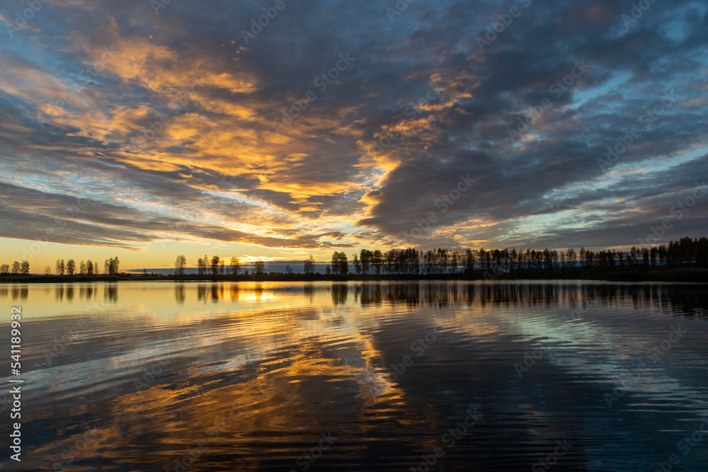 Beautiful lake at sunrise, golden hour sunrise, sunlight and grand cloud reflections on water, colorful dramatic sky at sunrise, dark silhouettes of trees, motion blur
