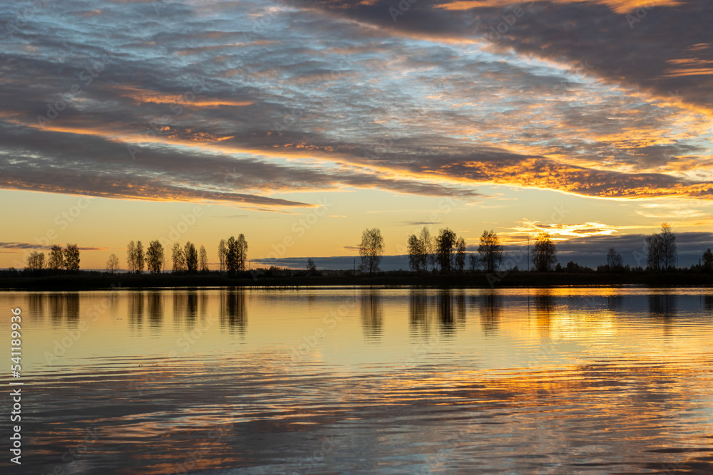 Beautiful lake at sunrise, golden hour sunrise, sunlight and grand cloud reflections on water, colorful dramatic sky at sunrise, dark silhouettes of trees, motion blur