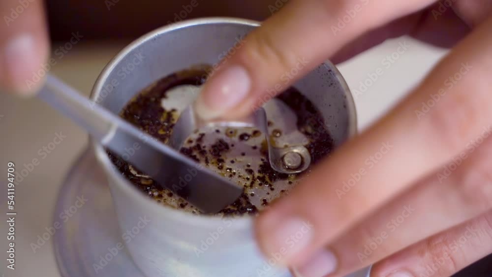 Barista's hand using metal spoon to press coffee on Vietnamese stainless steel coffee filter. Slow motion and close-up shot