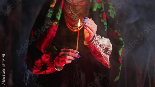Ukrainian woman praying with candle, she in traditional costume outdoors at night. Lady in authentic dress. Beauty of Ukraine, ethnic clothing, details.