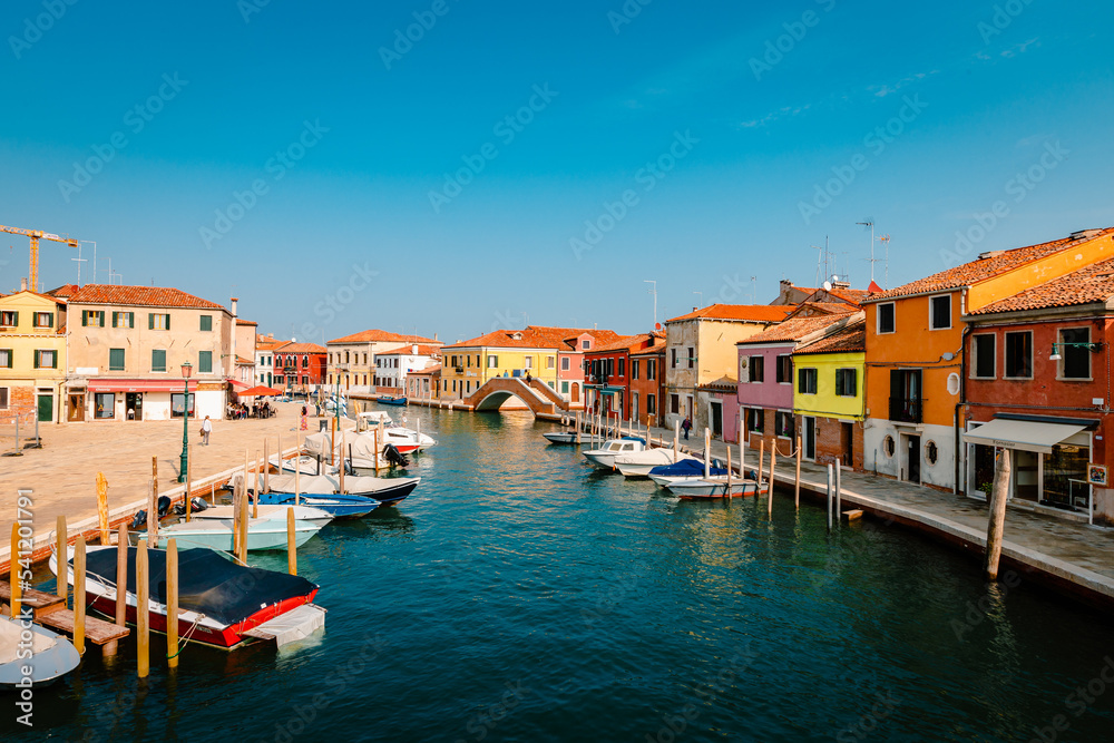 Murano canal with colorful houses, moored boats and tourist walking