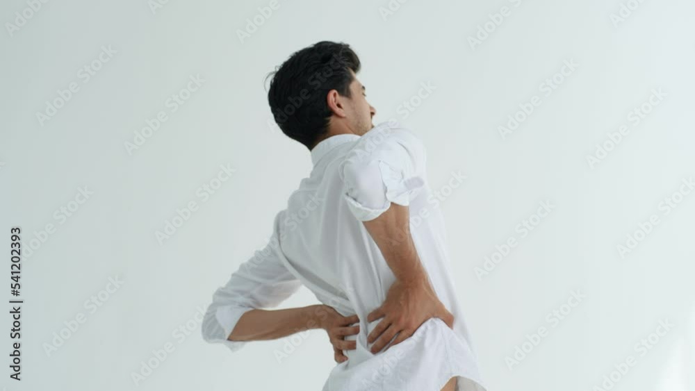 Studio portrait of unhealthy bearded man touching injured sore back, suffering lower lumbar discomfort, muscle pain of overwork, pinched nerve and grimacing on white isolated background, slow motion. Studio portrait of unhealthy bearded man touching injured sore back, suffering lower lumbar discomfort, muscle pain of overwork, pinched nerve and grimacing on white isolated background, slow motion.