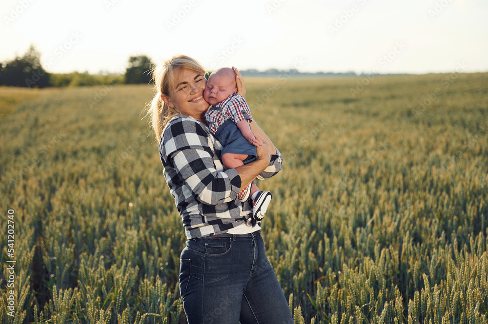Standing and smiling, Happy woman on the agricultural field is with little baby in the hands