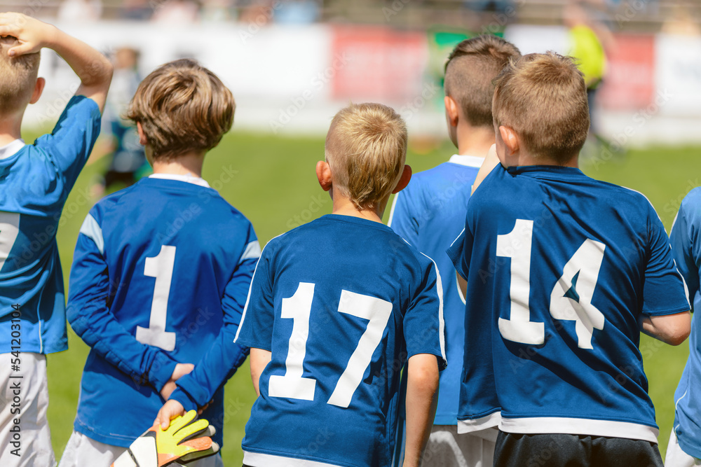 Fototapeta premium Football players wearing blue jersey shirts in the youth team. Boys in blue jersey shirts watching a tournament game. Group of kids in a school sports team