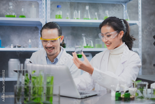 Female scientist is smiling and holding substance in glassware. Two people work in eco biology laboratory, Natural skin care, beauty products, Alternative herb or botany serum, Experiment of medical.