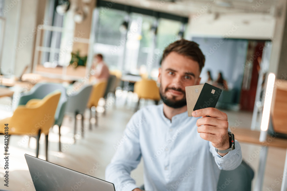 © standret - Holding credit cards. Young man is sitting in the cafe and working by using laptop © standret - Holding credit cards. Young man is sitting in the cafe and working by using laptop