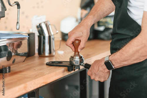 Busy by working with coffee machine. Cafe worker in white shirt and black apron is indoors