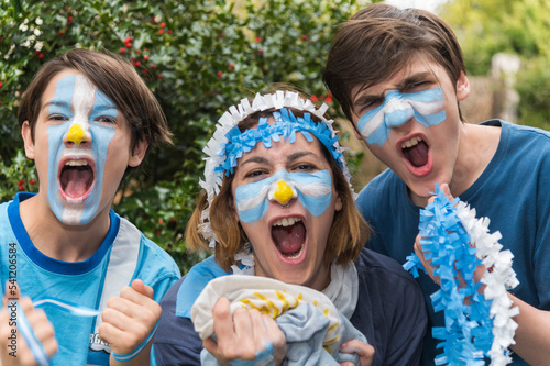 Familia con la cara pintada con los colores de la bandera Argentina  felices alentando al seleccionado en los partidos del mundial de futbol. 