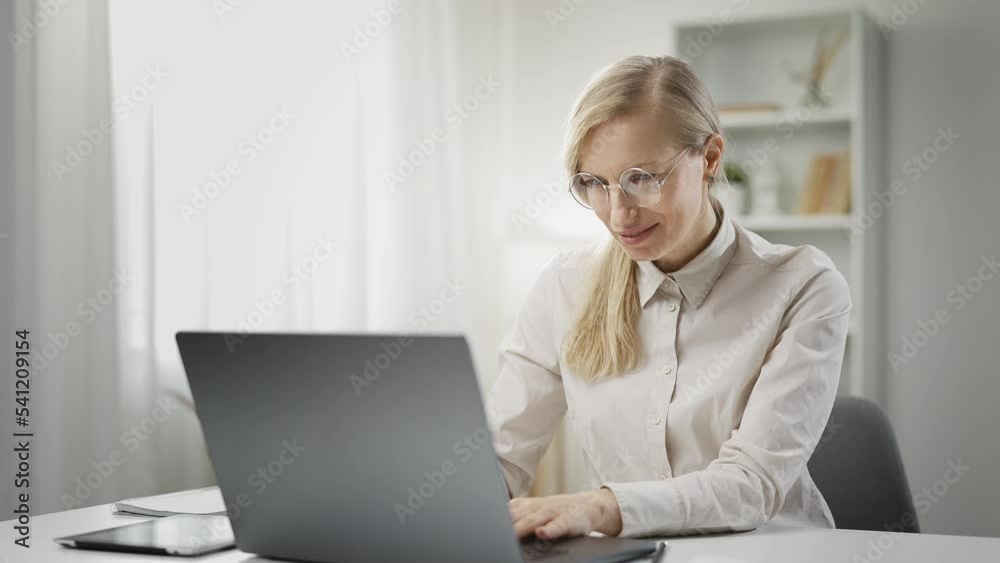 Smiling blond female working on laptop while staying at home, feeling satisfied with job done, remote employment Smiling blond female working on laptop while staying at home, feeling satisfied with job done, remote employment