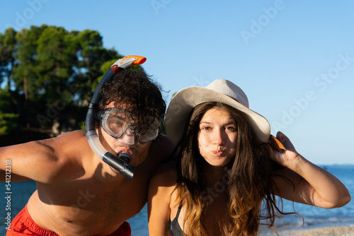 Happy young couple having fun on beach. Boyfriend with snorkeling mask giving piggy back ride to his girlfriend with hat, laughing and enjoying summer at sea.