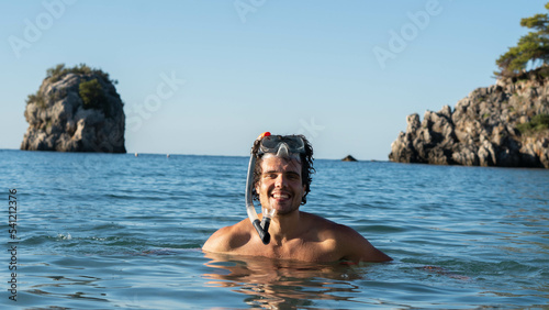 Şmiling attractive young man posing at the sea with the snorkeling mask in his hand.