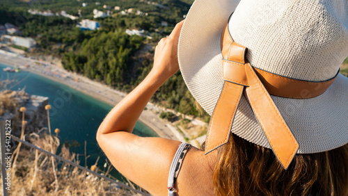 Young woman with hat looking in the direction of Valtos beach in Greece. Vacation, travel, summertime concept.