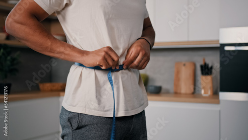 Unrecognizable sporty male sports man African guy measures waist with measuring tape check weight loss training workout sport dieting healthy nutrition control calories body muscle mass centimeters