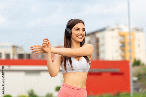 Athletic young woman with towel smiling and streaching. Young sporty woman training. Woman Doing Workout Exercises On Street . Fit girl streaching before active fitness training