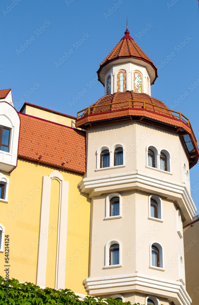 beautiful tower of small castle against the blue sky. Architecture of buildings. Red cone-shaped roof. Arched windows.