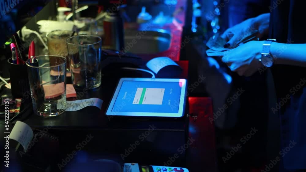 The seller in a nightclub counts money at the checkout during a party, light music. The seller in a nightclub counts money at the checkout during a party, light music.